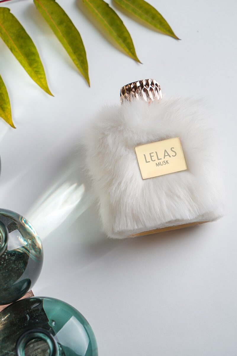Furry white perfume bottle with gold accents and leaves.